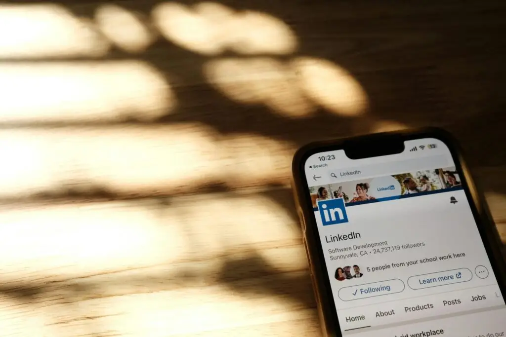 Smartphone mit geöffneter LinkedIn-Unternehmensseite auf einem Holztisch – Einstieg ins LinkedIn Marketing